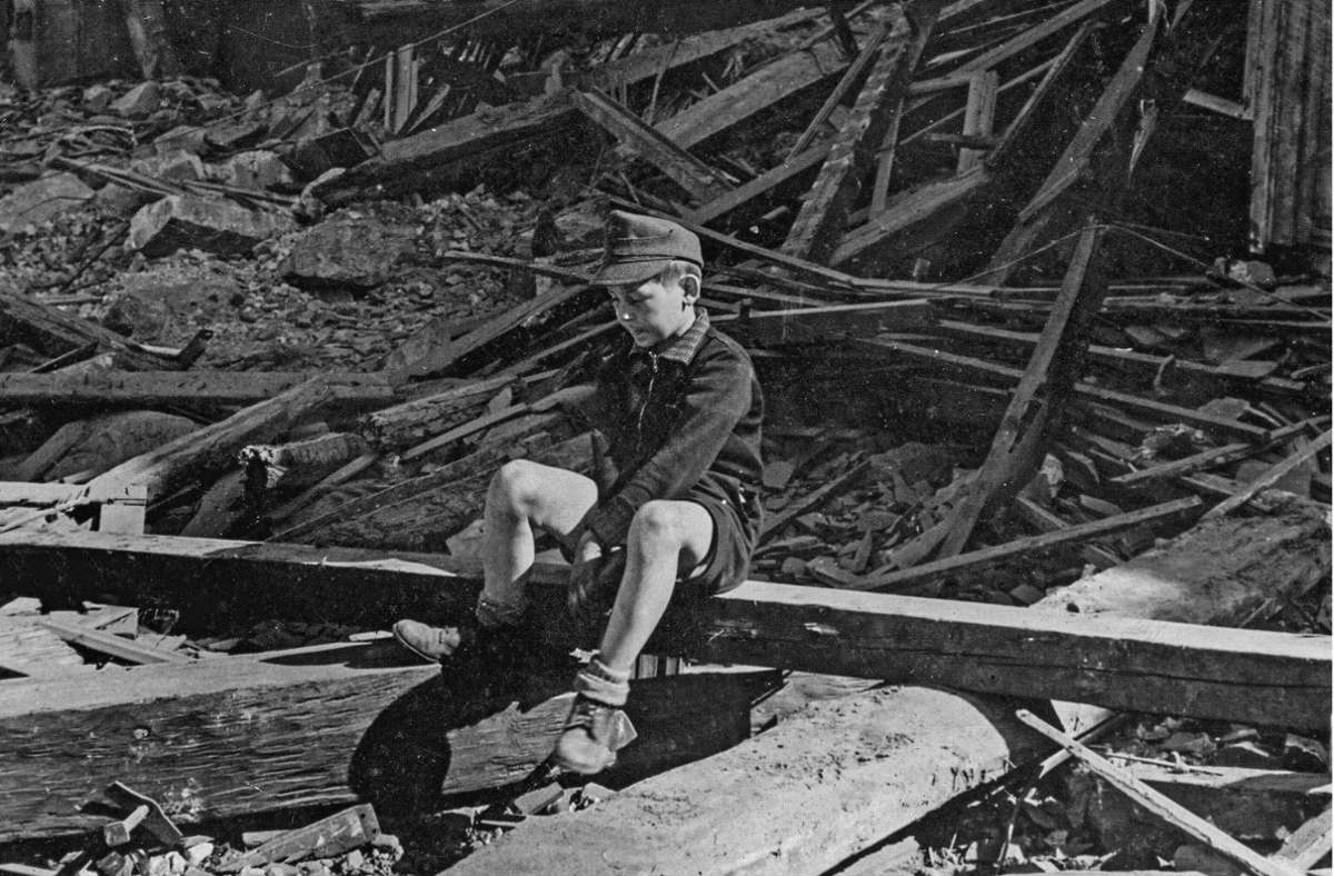 Ein Junge sitzt im März 1945 vor einem zerstörten  Wohnhaus in einem unbekannten deutschen Ort.
