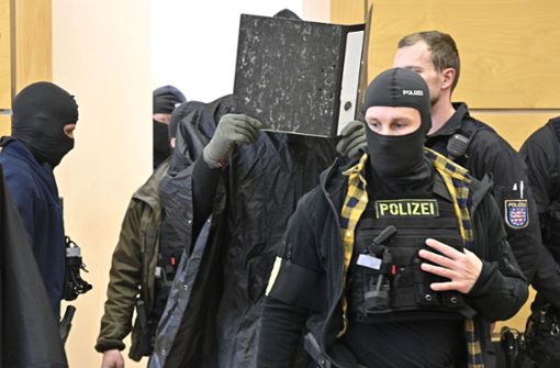In Regencape und Handschuhen, einen Aktenordner vor dem Gesicht: der Angeklagte. Foto: /Heiko Matz