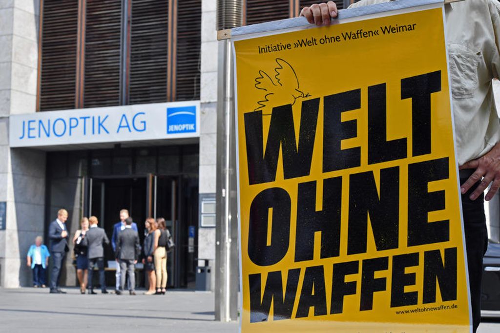Vor Beginn der Hauptversammlung der Jenoptik AG steht ein Demonstrant mit einem Plakat mit der Aufschrift "Welt ohne Waffen" an der Weimarhalle in Weimar. Foto: Martin Schutt, dpa