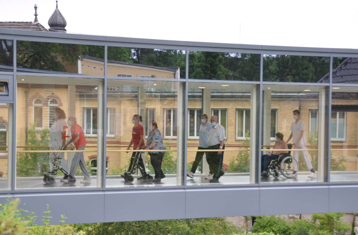 Begleitet von Pflegekräften wechseln die Reha-Patienten über die gläserne Brücke vom Haupthaus der Geriatrischen Fachklinik Georgenhaus in Haus 8. Foto: /Ralph W. Meyer