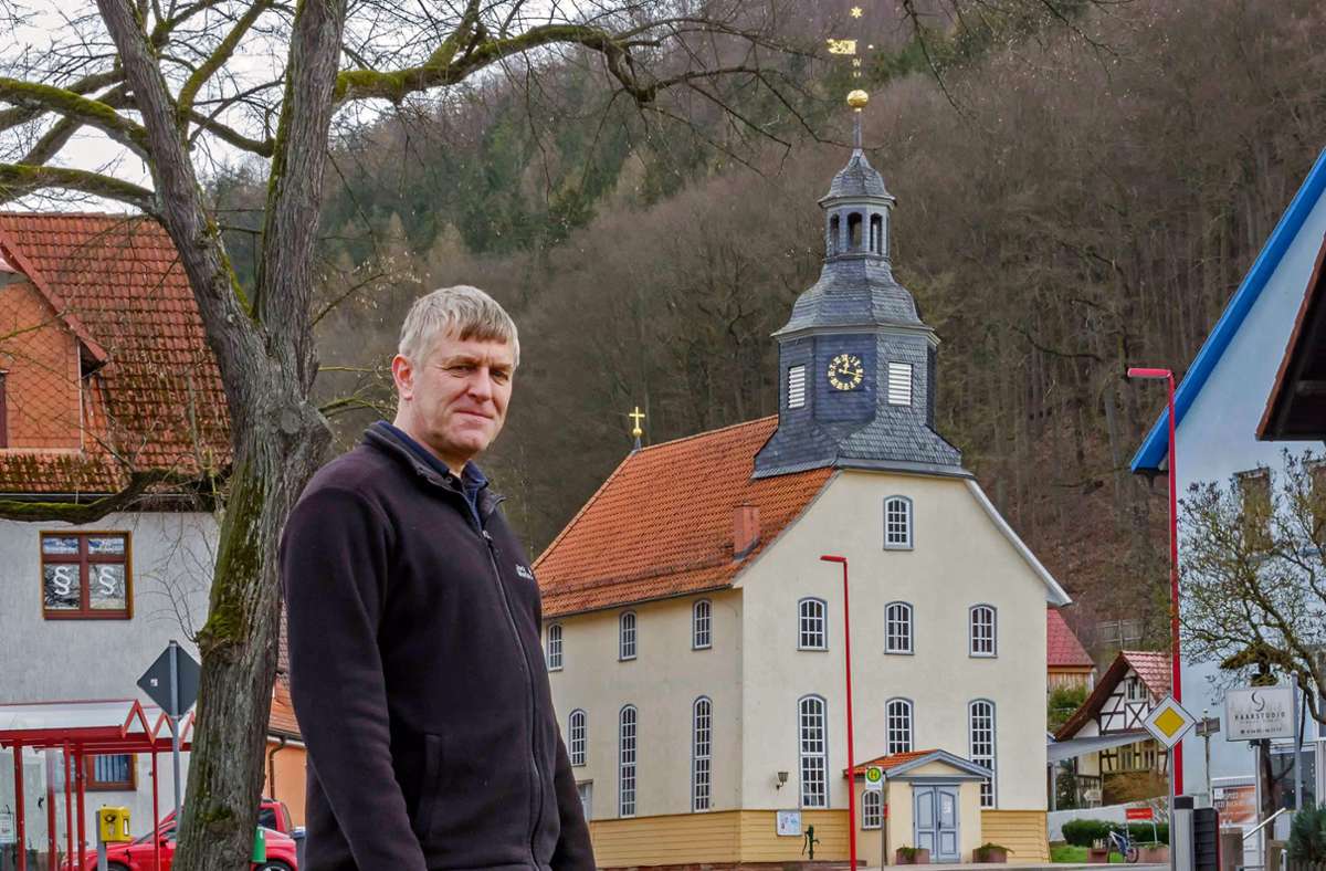 Pfarrer Olaf Schnarr, im Hintergrund die Asbacher Dorfkirche, die in diesem Jahr 300 Jahre alt wird.